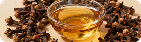 Dried cloves around a small bowl of golden oil